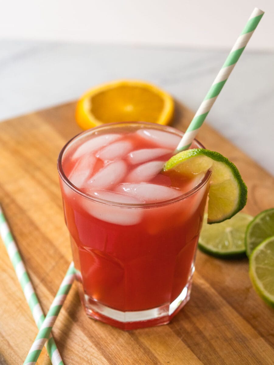 Watermelon margarita with lime wedges and straws on a wooden cutting board.