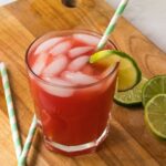A glass of watermelon juice with lime slices and straws.