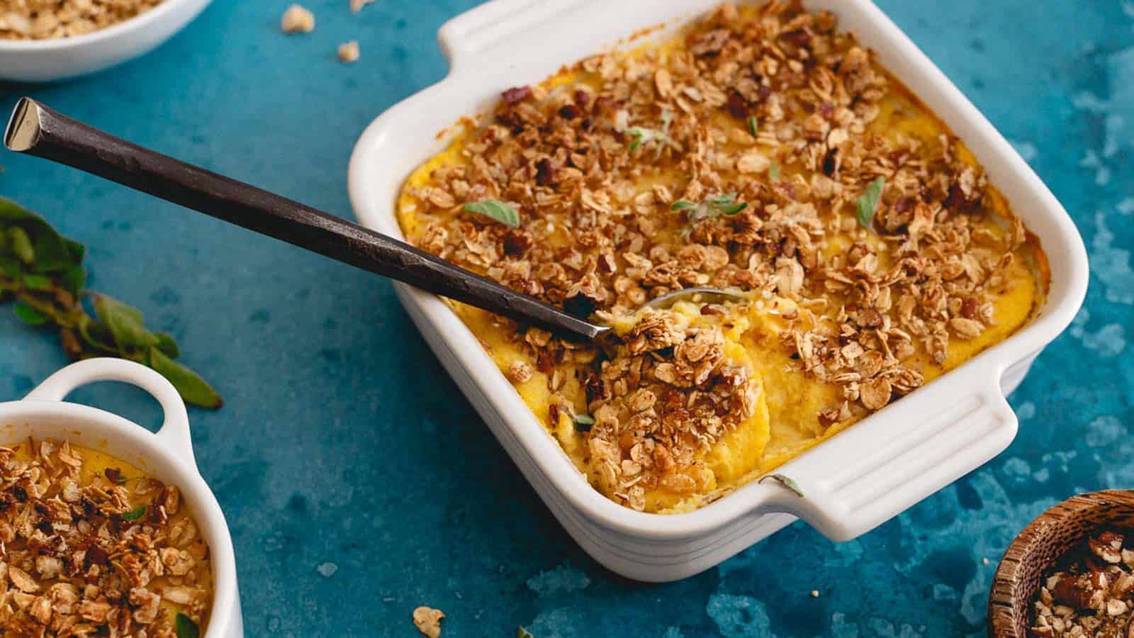 Creamy pumpkin cauliflower mash topped with savory granola and sage leaves in a white baking dish.