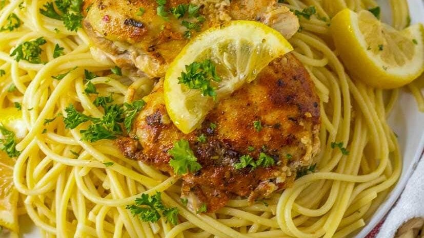 A plate of spaghetti with chicken and lemons on it.