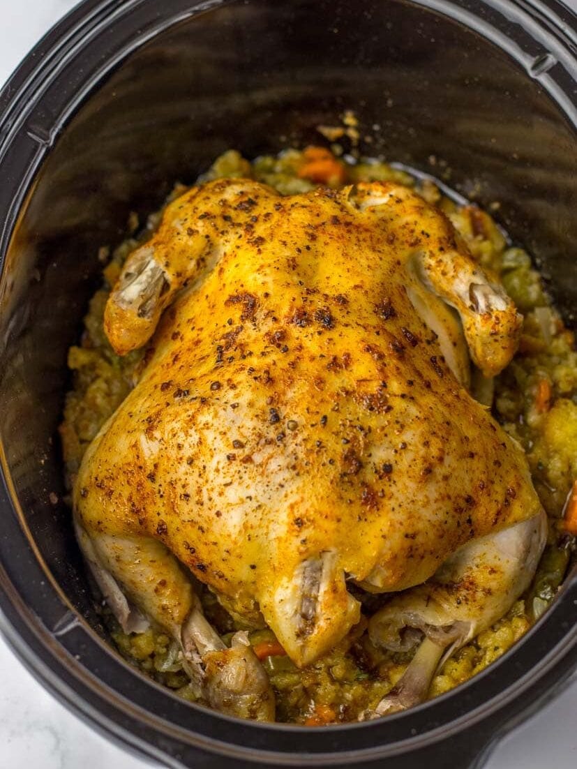 A chicken in a slow cooker with carrots and potatoes.