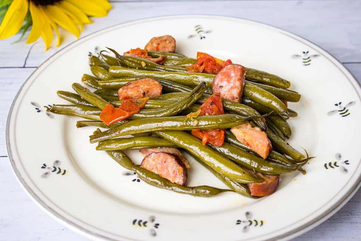 Green beans with sausage on a white plate.