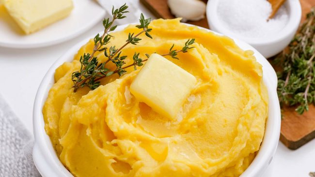 Image of a bowl of squash mashed potatoes with a pat of butter and a sprig of thyme on top.