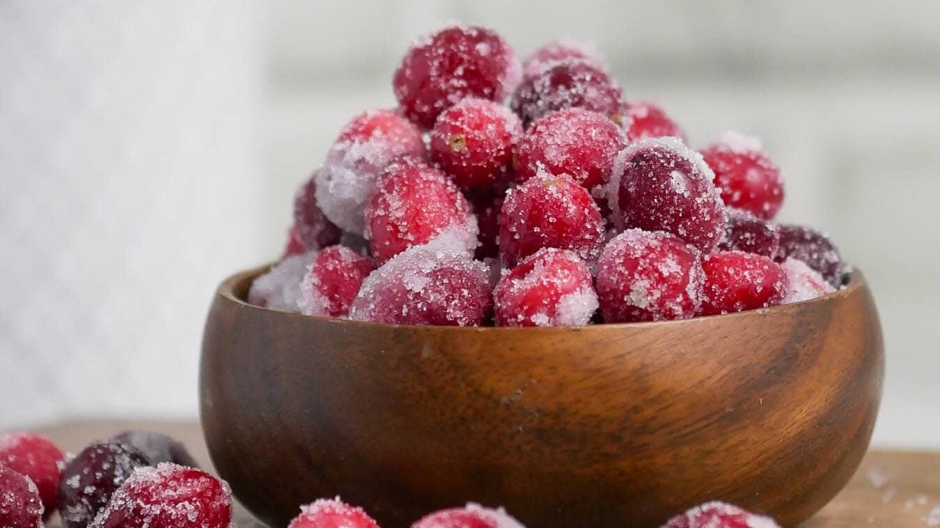 Sugared cranberries in a wooden bowl on a wooden table.