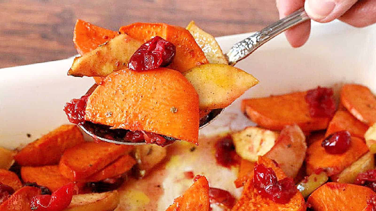 A spoonful of sweet potato slices with apples and cranberries in a white dish.