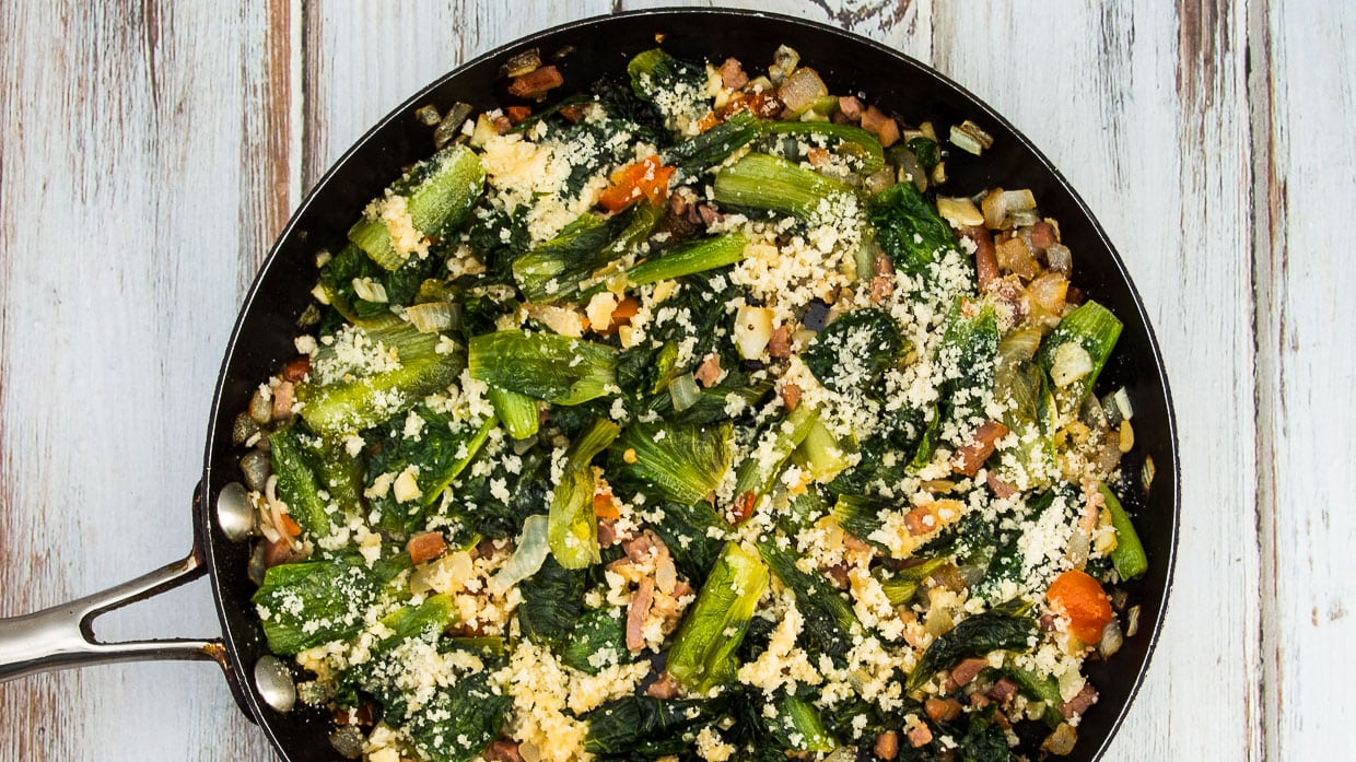 Top view of Utica Greens in a skillet with breadcrumbs and cherry peppers.
