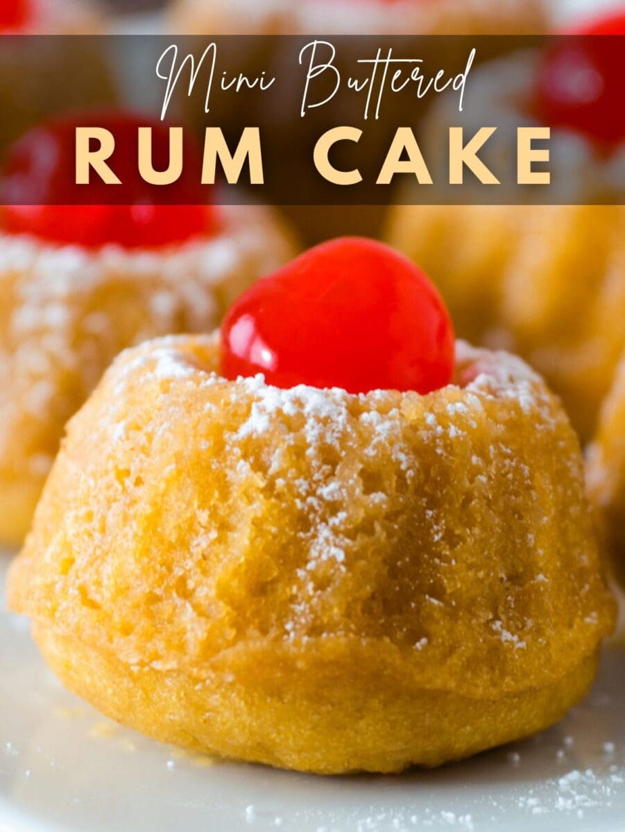 Close-up of a mini rum cake topped with a red cherry and dusted with powdered sugar, with the text "Mini Buttered Rum Cake" overlaid at the top.
