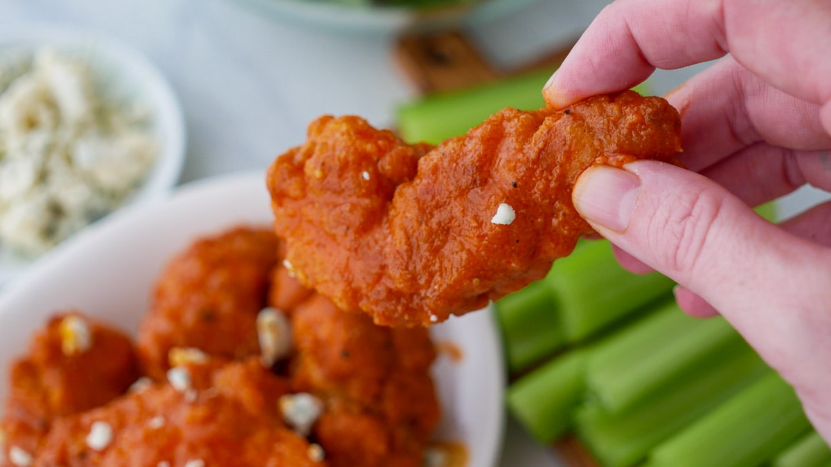 A person holding buffalo wings in front of a plate of celery.