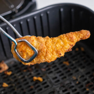 A piece of chicken being pulled out of an air fryer.