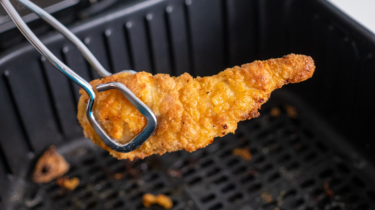 A piece of fried chicken being pulled out of an air fryer.