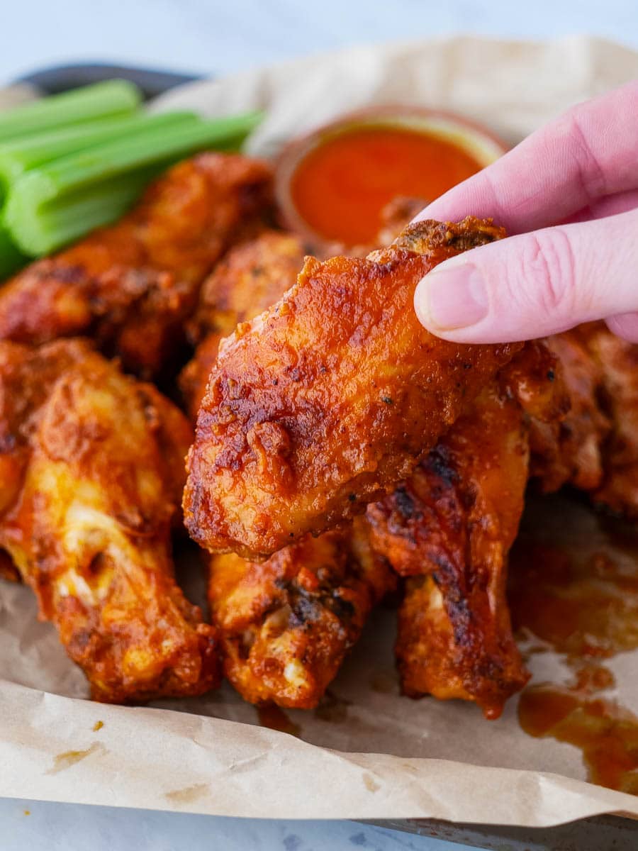 A hand is holding a tray of buffalo wings.