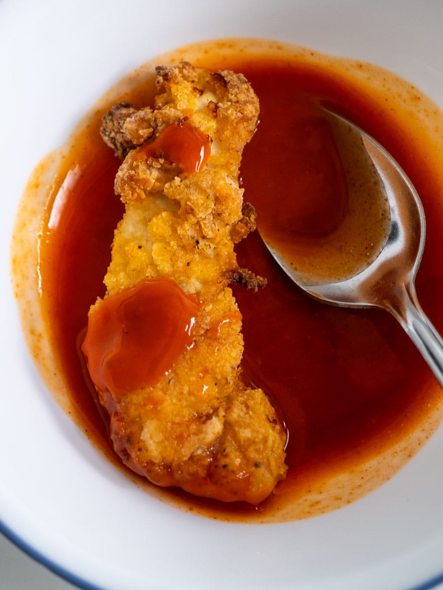 A bowl of chicken tenders in a spicy buffalo sauce, ready to be enjoyed with a spoon.