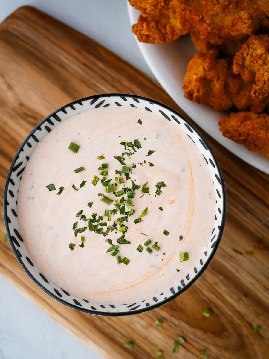 A bowl of dip with fried chicken on a cutting board.