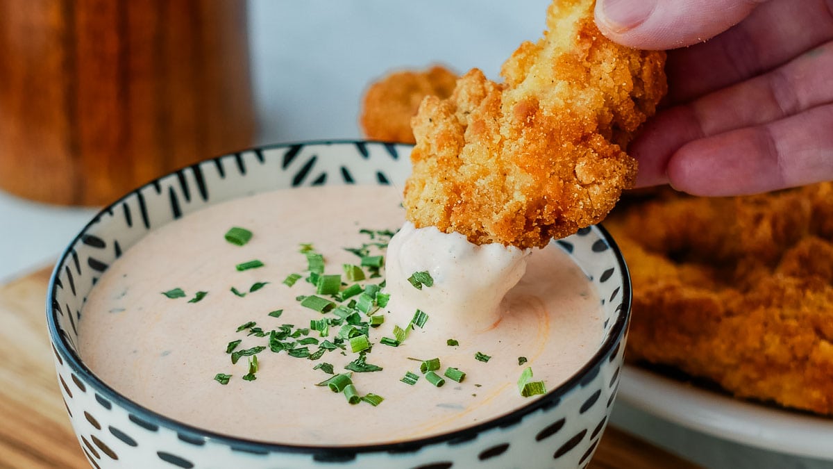A person dipping chicken fingers into a bowl of dip.