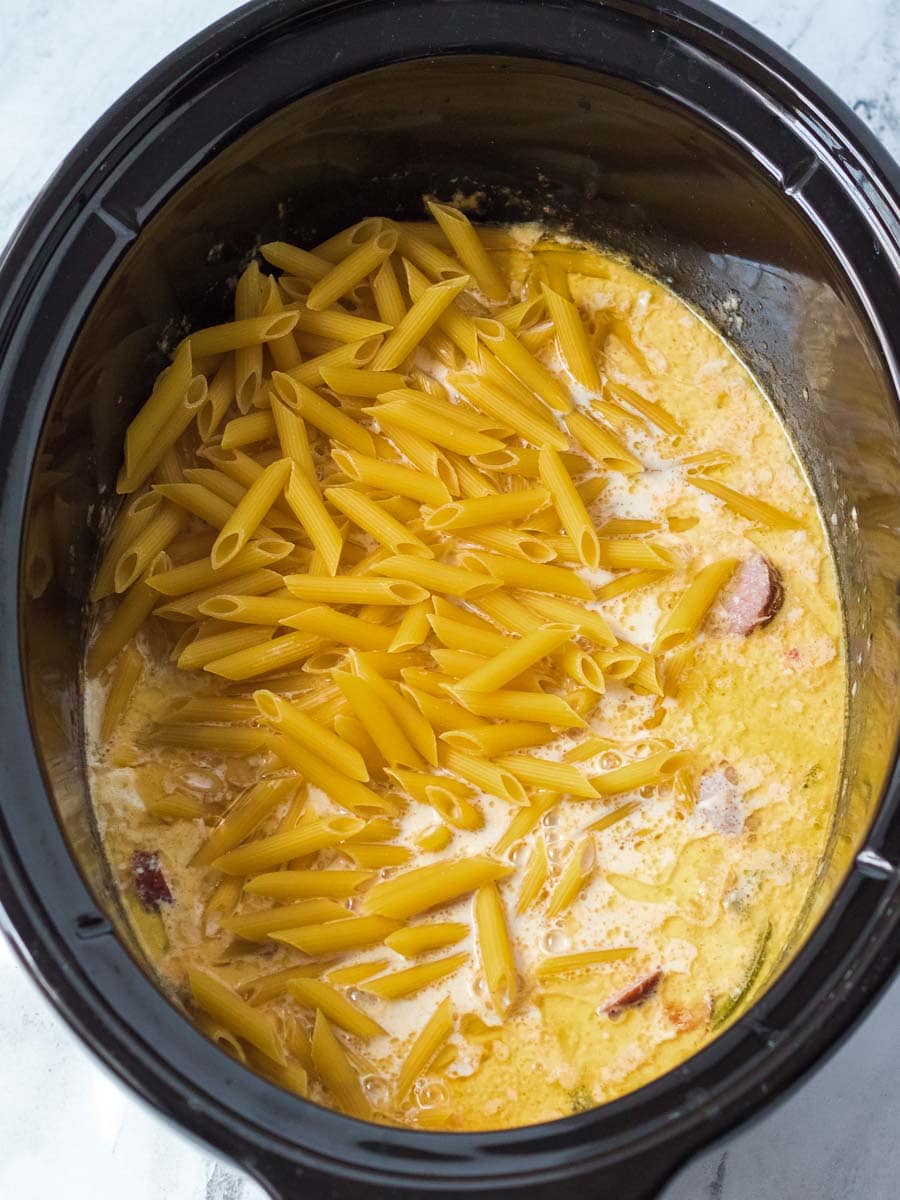 A crock pot filled with pasta and ham.