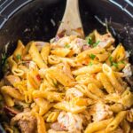 Chicken and pasta in a slow cooker with a wooden spoon.