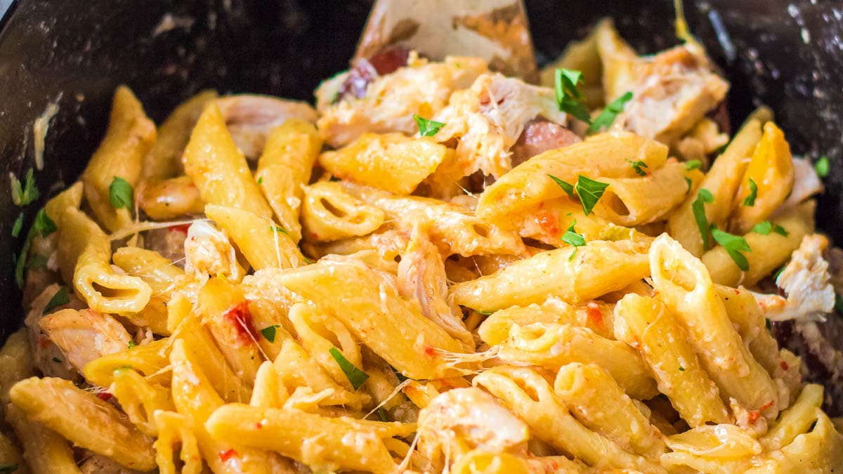 Chicken and pasta in a slow cooker with a wooden spoon.