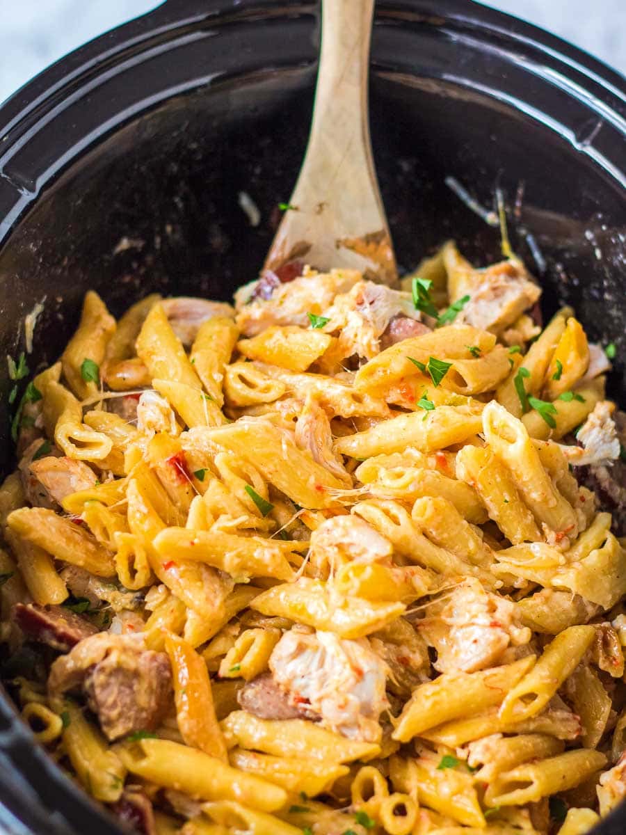 A crock pot filled with pasta and chicken.