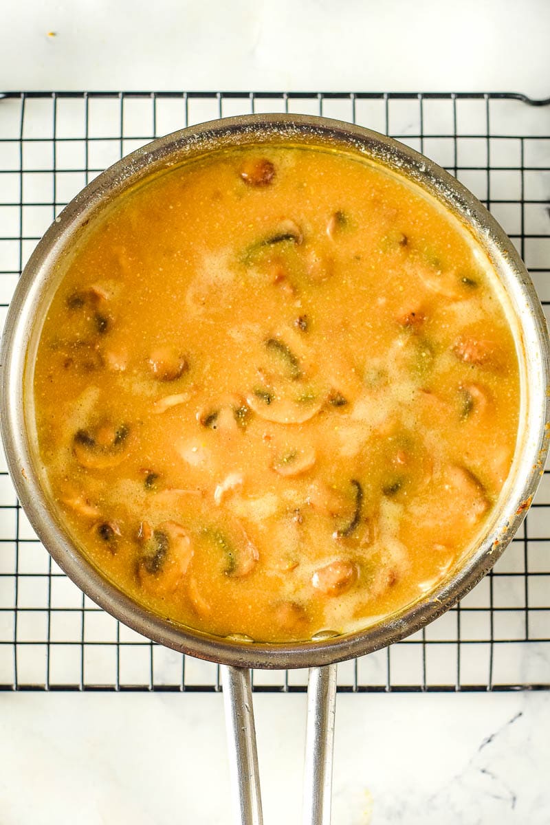 A pan of soup with mushrooms in it on a cooling rack, possibly chicken stroganoff flavored.