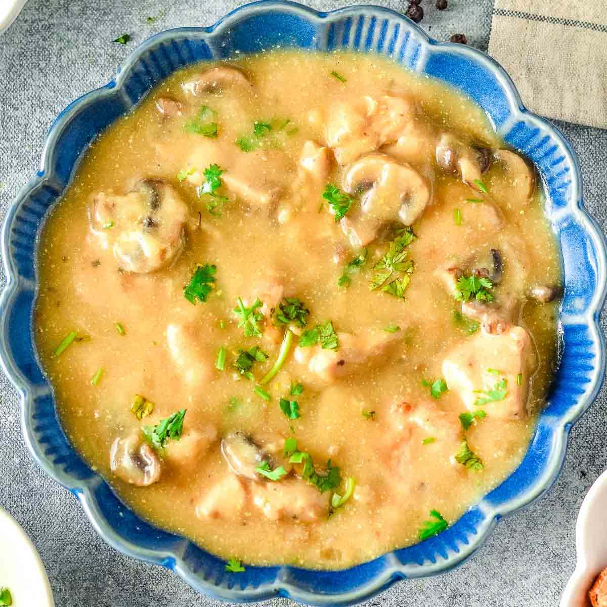 A bowl of chicken stroganoff with bread and parsley.