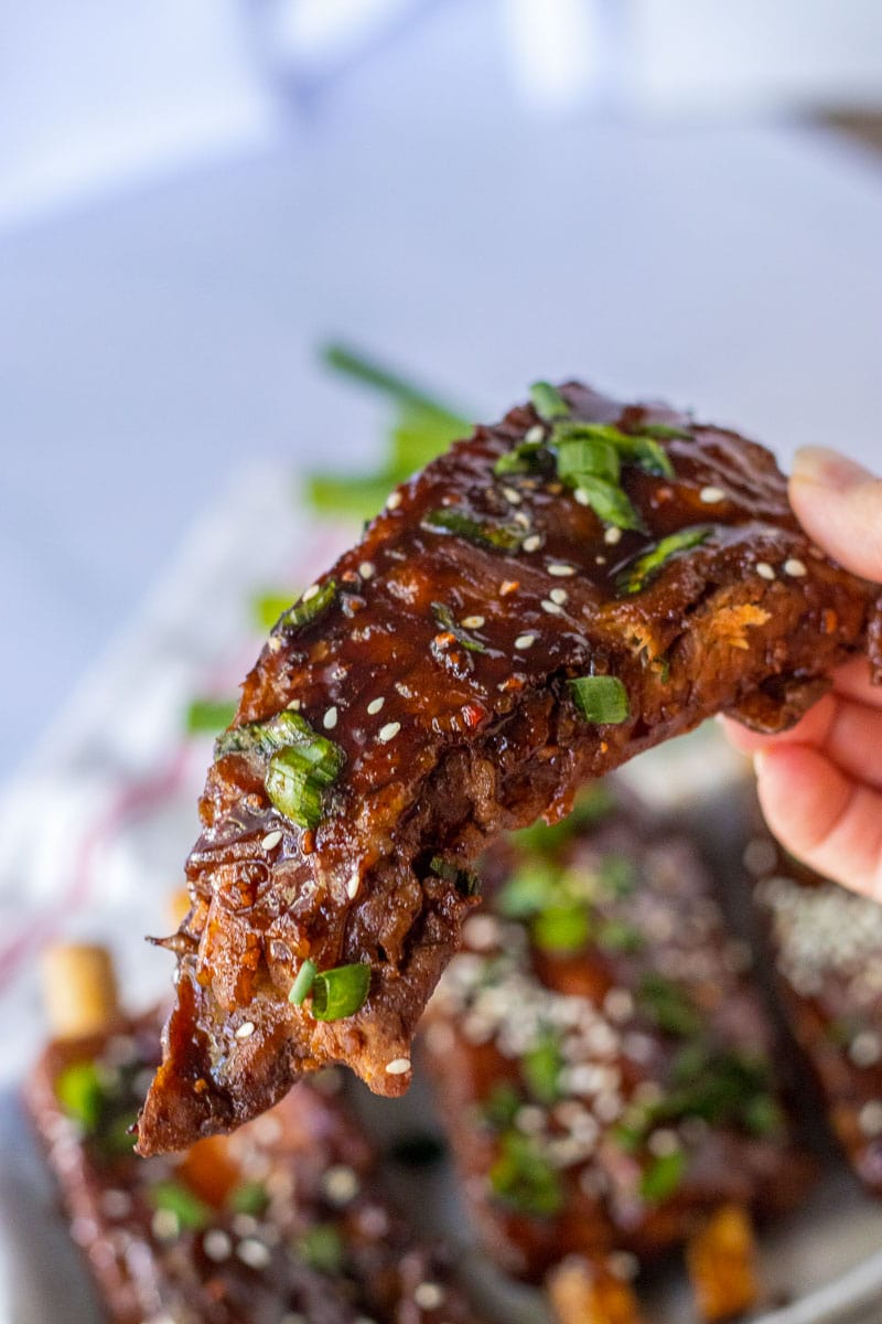 A person holding a piece of ribs with sesame seeds.