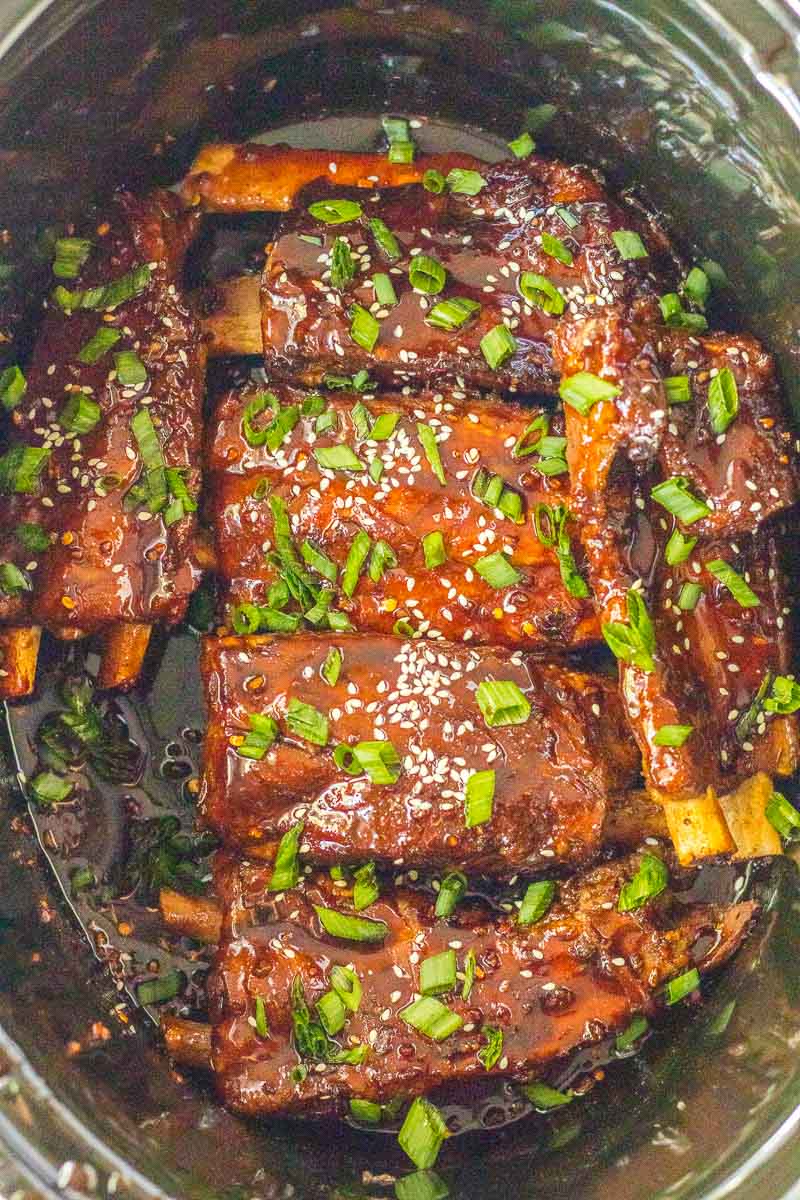 A slow cooker full of ribs with sauce.