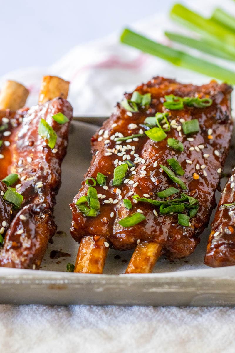 Asian ribs on a plate with green onions and sesame seeds.