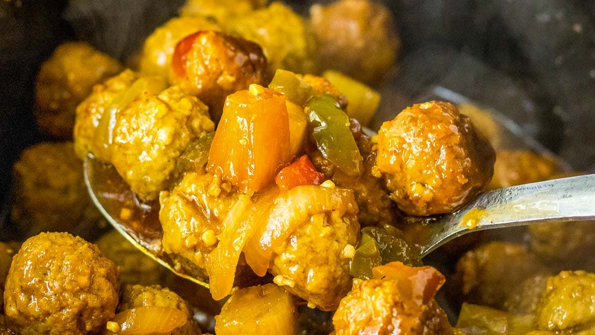 A spoonful of meatballs and vegetables in a slow cooker.