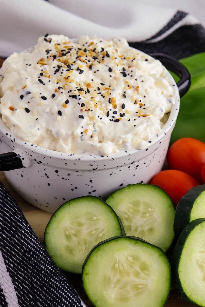 A bowl of dip with cucumbers and tomatoes.
