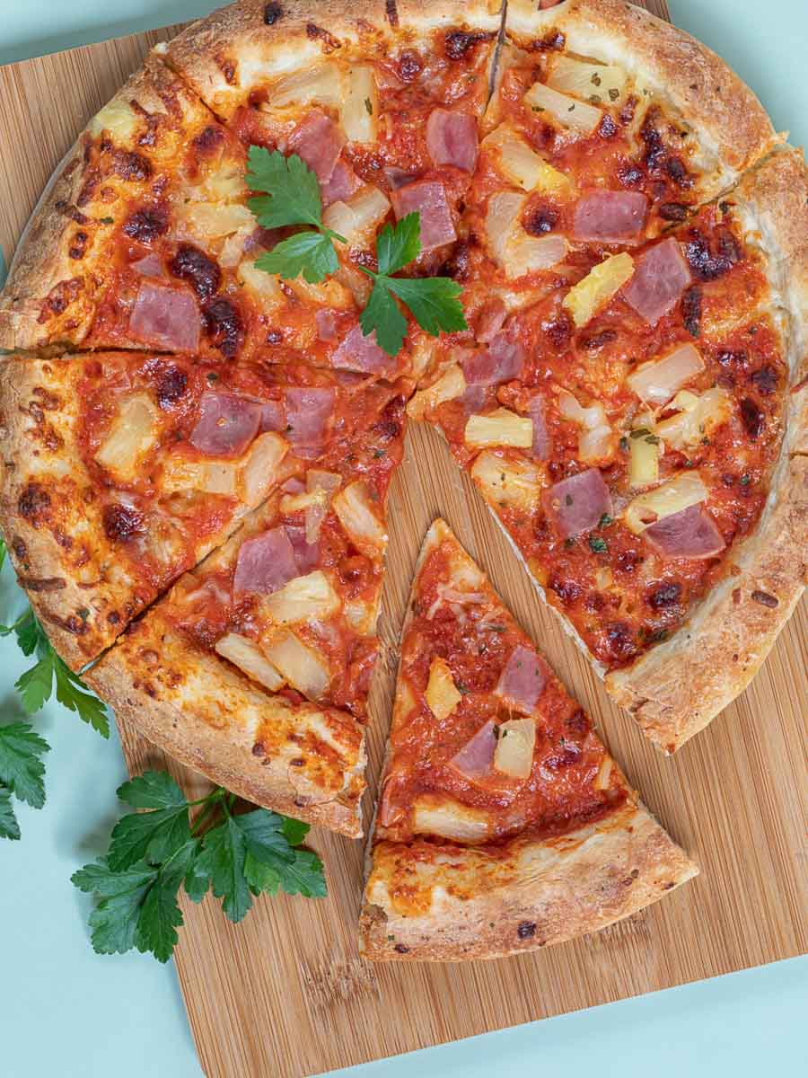 A upgraded frozen pizza with ham and pineapple on a wooden cutting board.