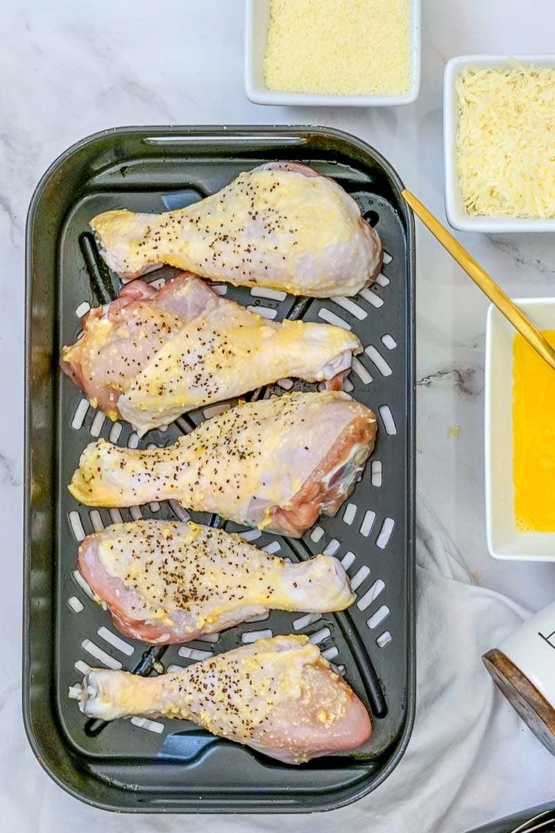 A baking tray with chicken legs and cheese on it.