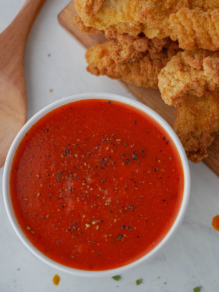 A bowl of tomato sauce with fried chicken on a cutting board.
