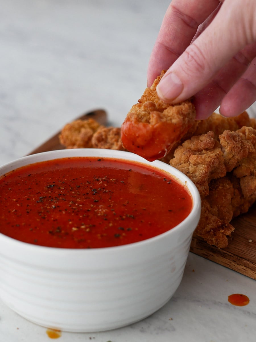 A person dipping chicken wings into a bowl of tomato sauce.