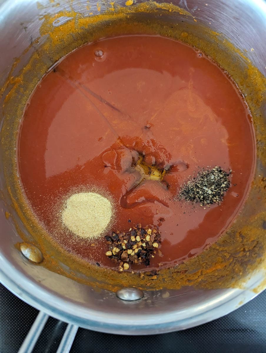 A pot of tomato sauce with spices and seasonings.