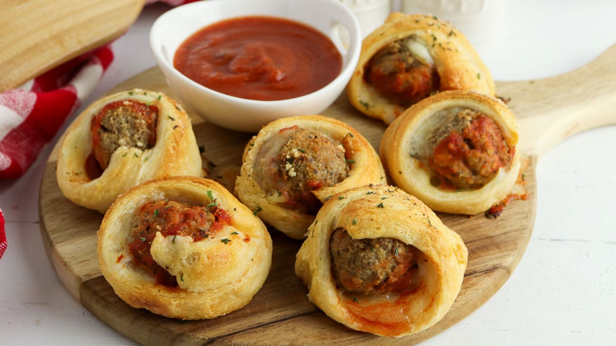 Meatball crescents with dipping sauce on a wooden cutting board.