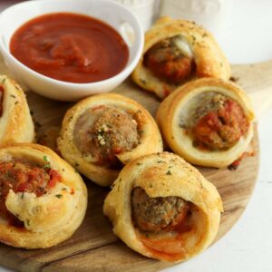 Meatballs wrapped in dough on a wooden cutting board.