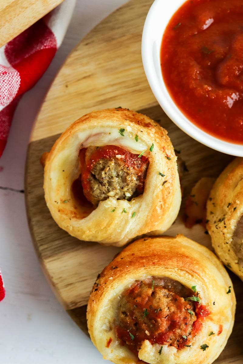 Meatball crescent rolls with tomato sauce on a wooden cutting board.