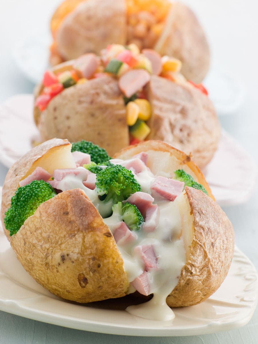 A plate of baked potatoes with ham, broccoli, and cheese.