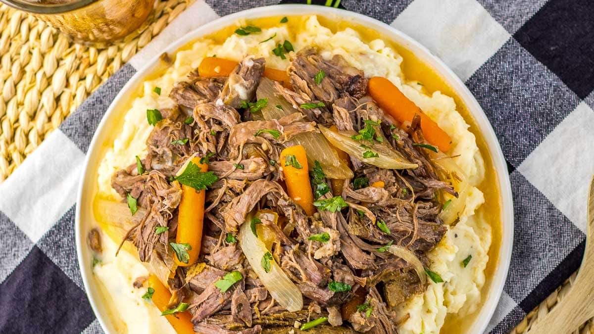 A plate of pot roast with carrots and mashed potatoes.