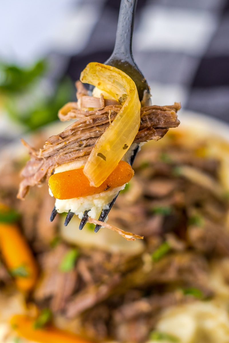 A fork is holding a piece of beef with carrots and potatoes.