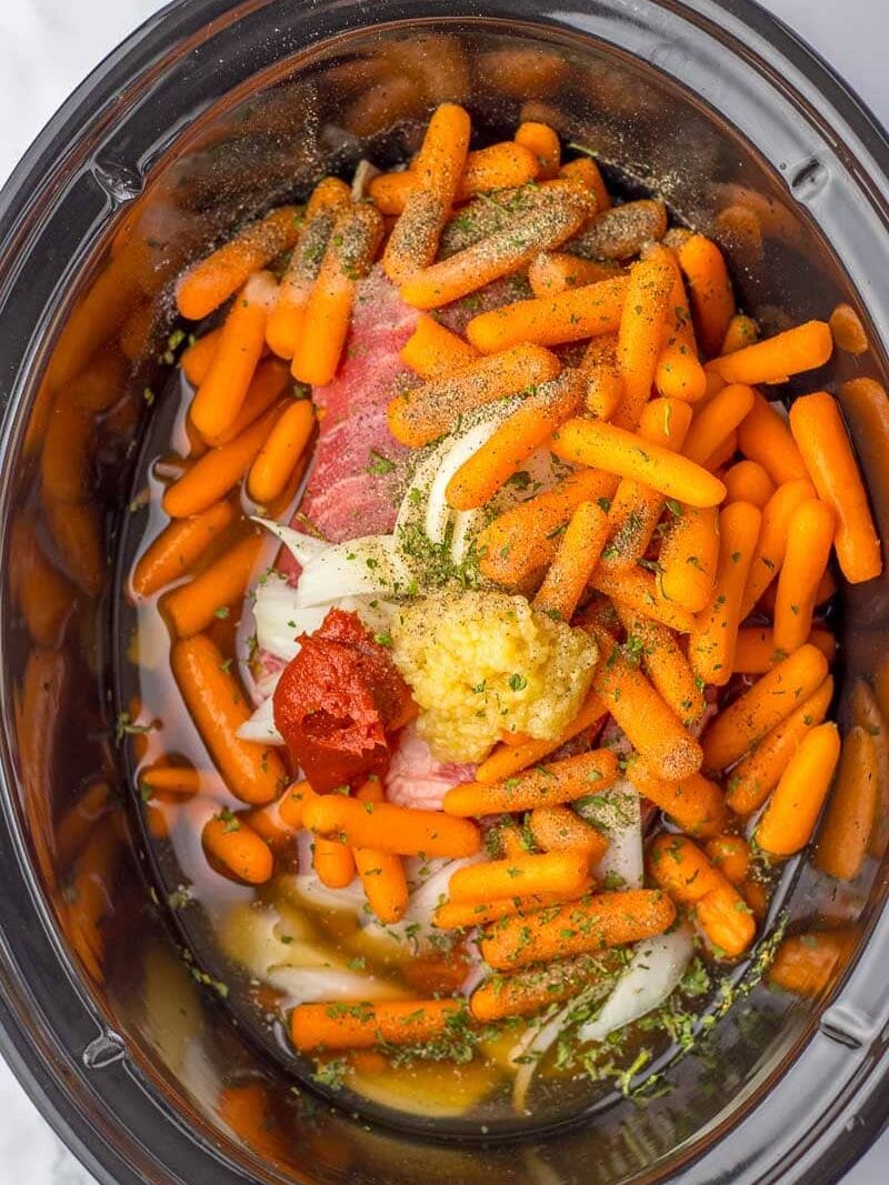 A crock pot filled with carrots and meat.