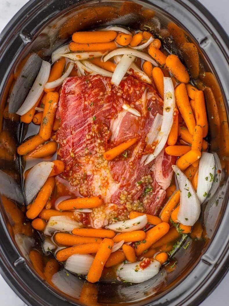 A slow cooker filled with meat, carrots and onions.