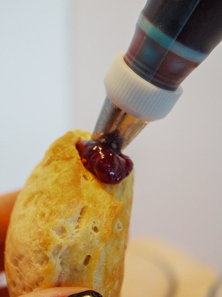 A person is putting jelly inside a donut using pastry bag.