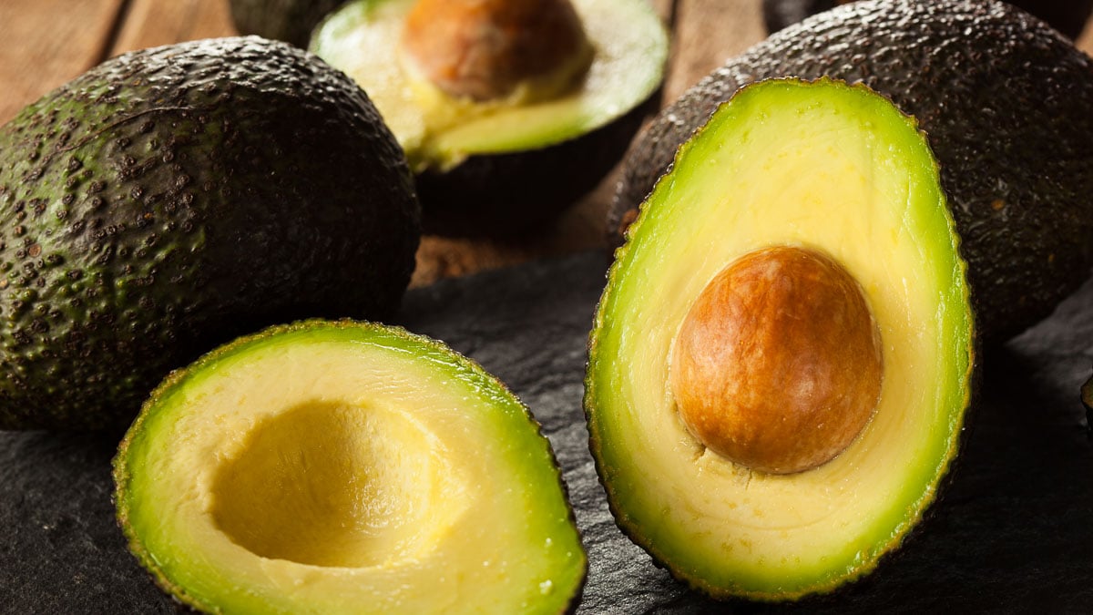 Avocados cut in half on a wooden table - includes information about how to buy avocados.