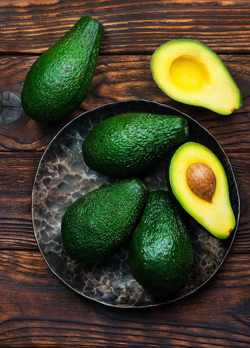 Avocados on a plate on a wooden table showcasing how to buy avocados.