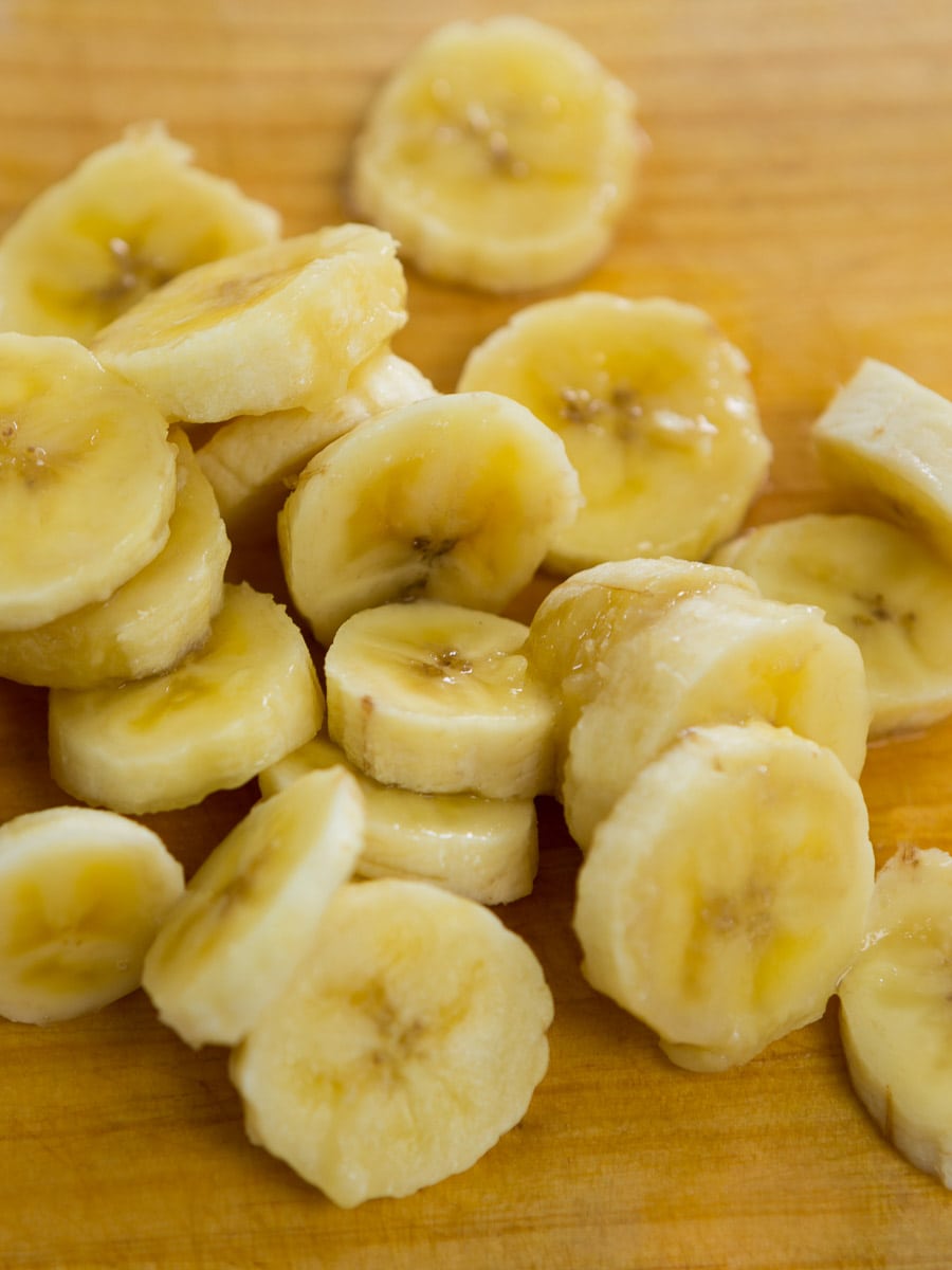 A pile of sliced bananas on a wooden cutting board, demonstrating how to store bananas by preparing them for future use.