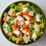 A bowl of Buffalo chicken caesar salad with dressing.