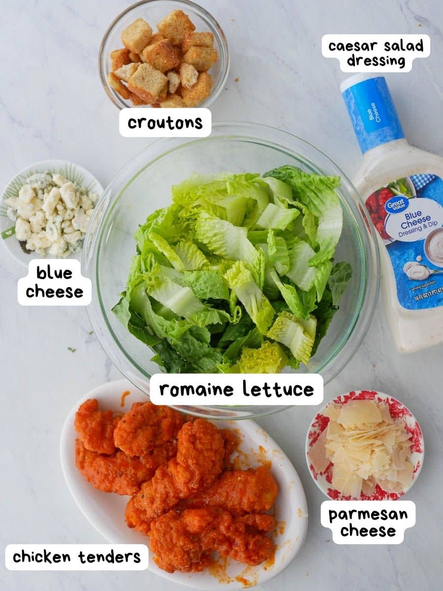 The ingredients for a chicken salad are shown on a marble countertop.
