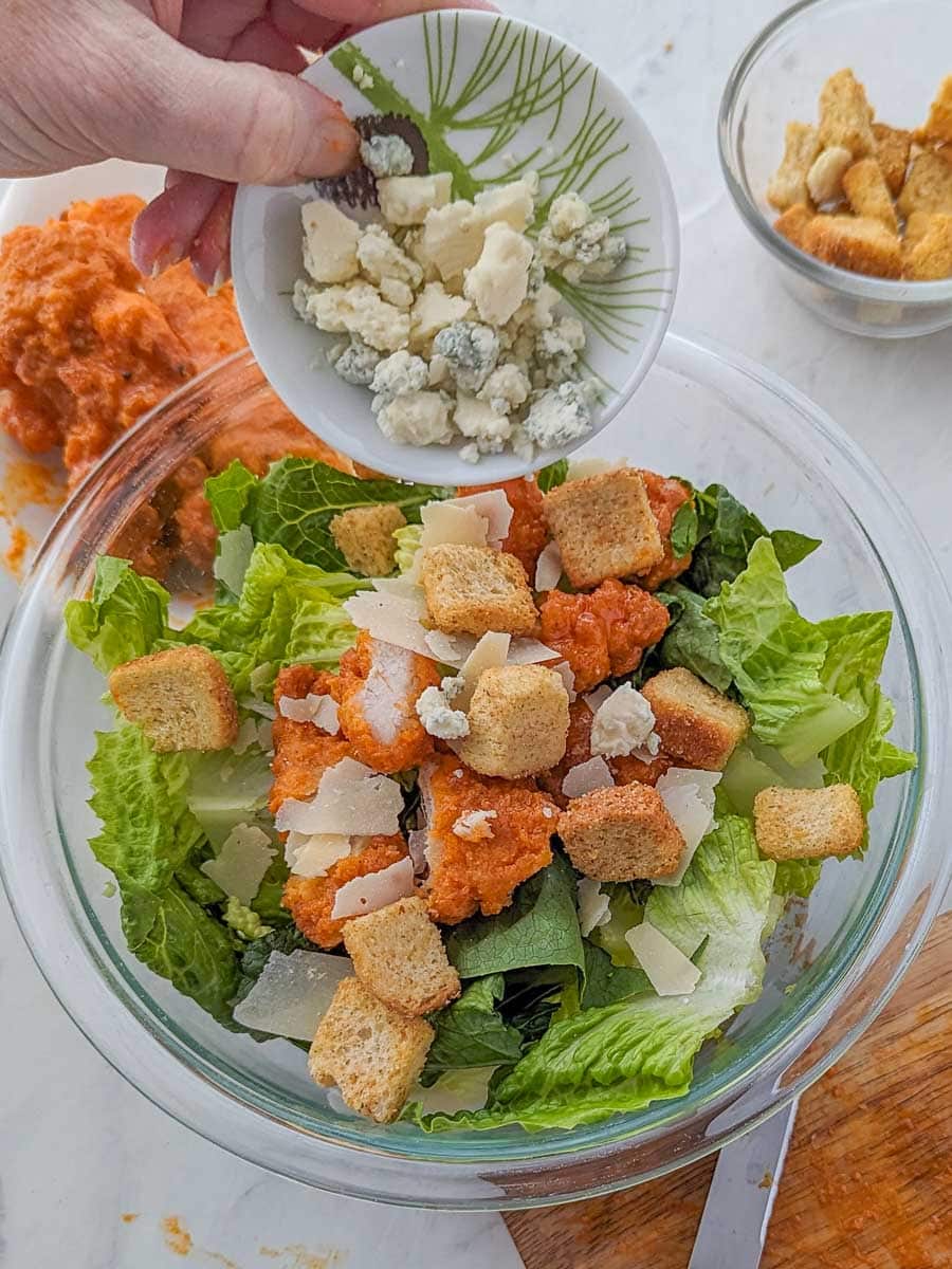 A person drizzling blue cheese on a salad.