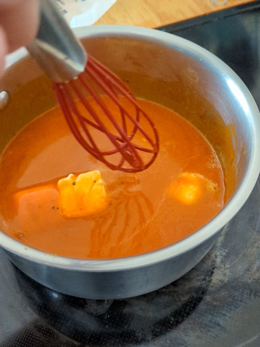 A person is whisking a sauce in a pan.